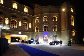 A grand building with arched windows and a blue carpet leading to a car display.