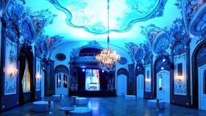 Un vaste hall doté d’un plafond et de murs richement décorés, d’un lustre et de plusieurs tables rondes.