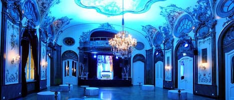 A grand hall with ornate ceiling and walls, a chandelier, and multiple round tables.