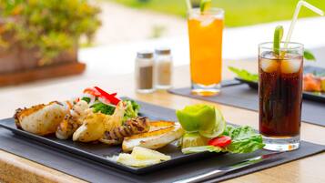 Una comida con mariscos a la parrilla y verduras, un vaso de té helado y una bebida adornada con lima sobre una mesa de madera.