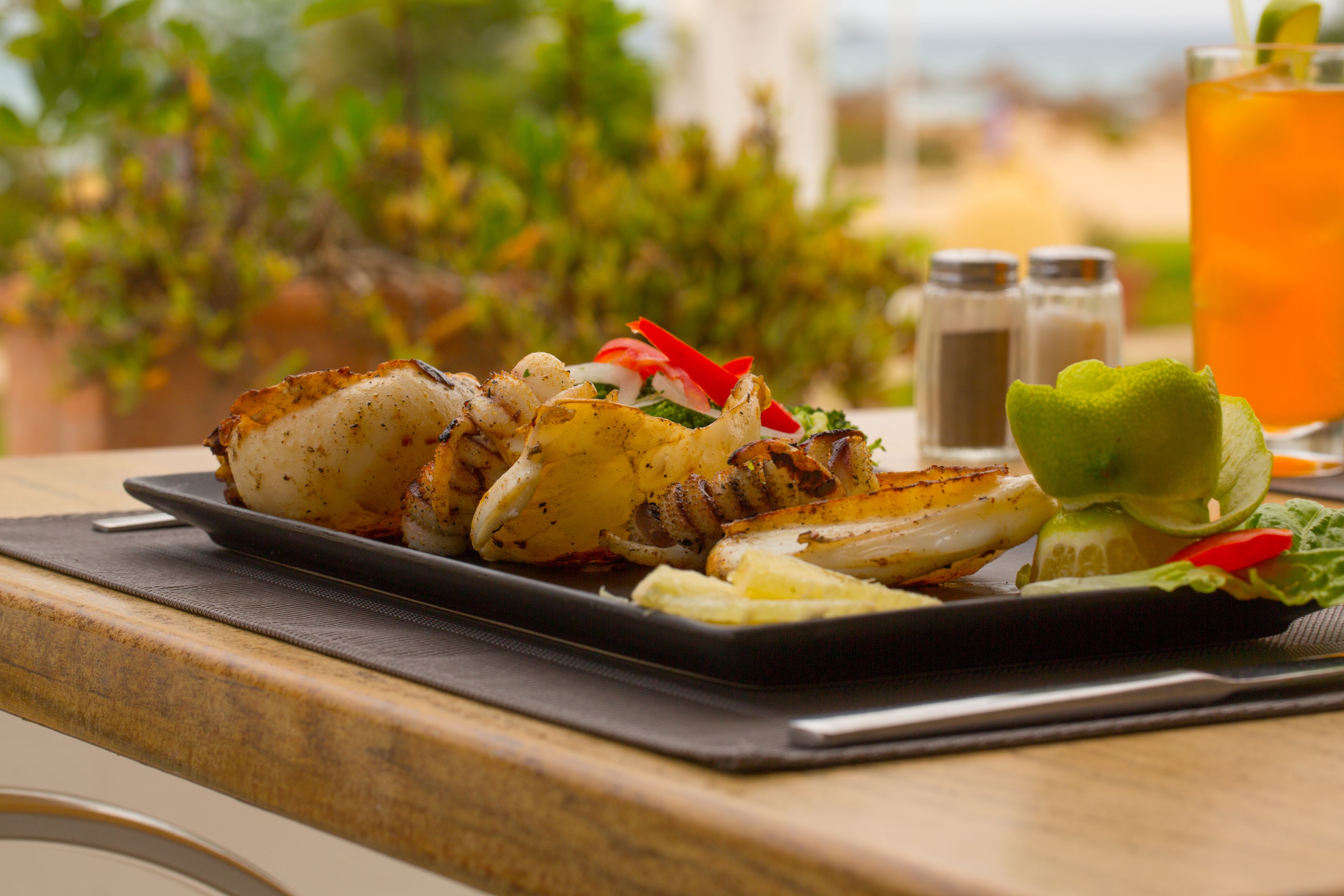 Une assiette de fruits de mer grillés, accompagnée de légumes et d’une boisson, est posée sur une table.