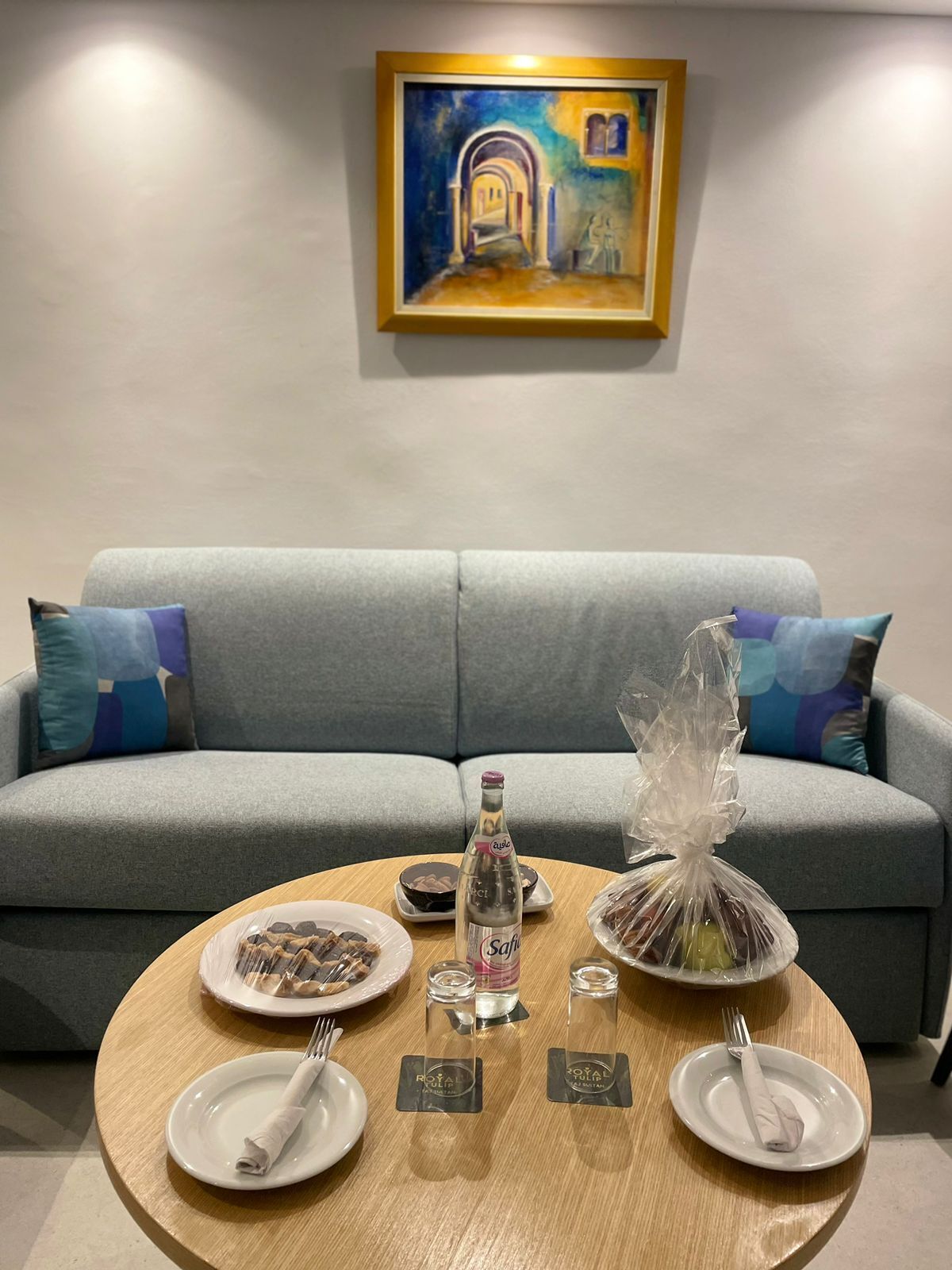 A dining setup with a round table, plates, cutlery, and a bottle of water.