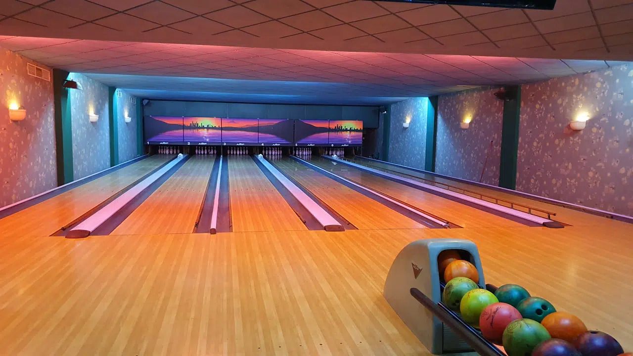 A bowling alley with multiple lanes, a bowling ball return, and a wall with a cityscape mural.