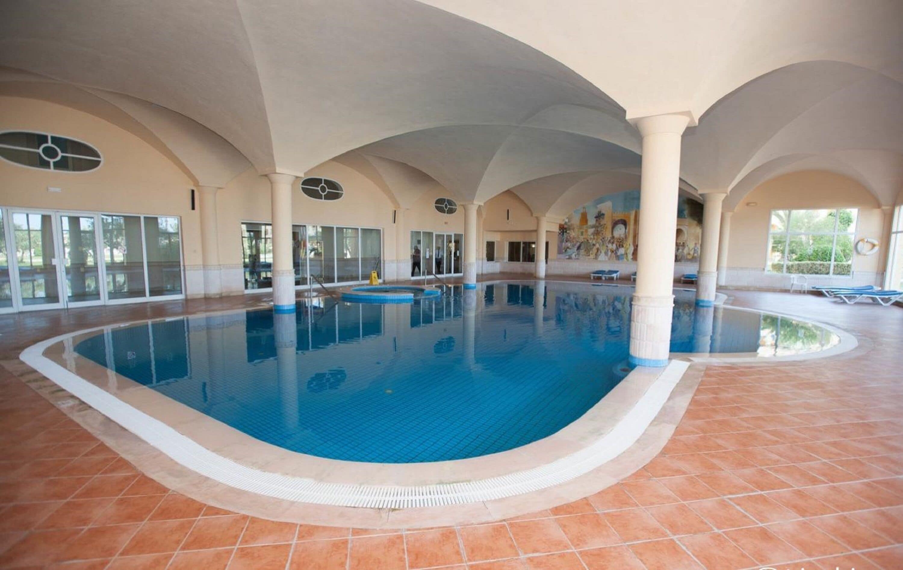 Una piscina techada, una piscina al aire libre, sombrillas