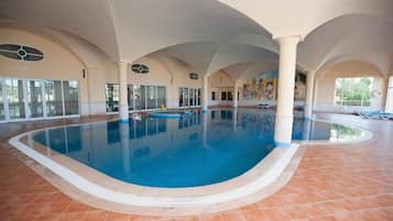 Una piscina techada, una piscina al aire libre, sombrillas