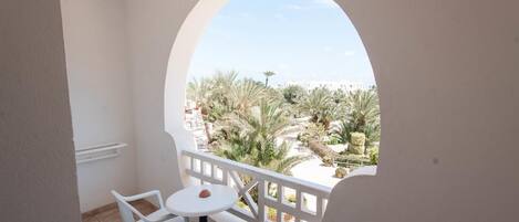 A balcony with a white table and chairs, a view of palm trees and a building in the background.
