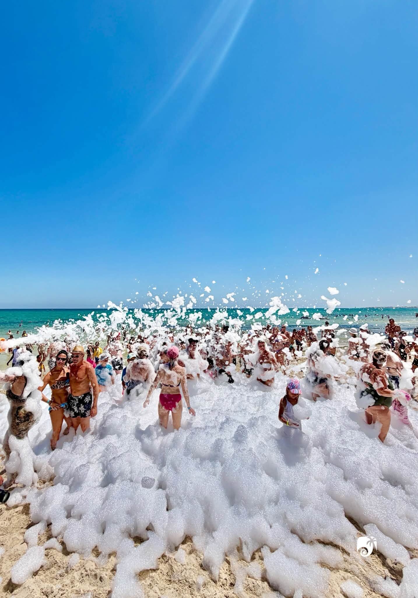 Escena de playa con gente cubierta de espuma.