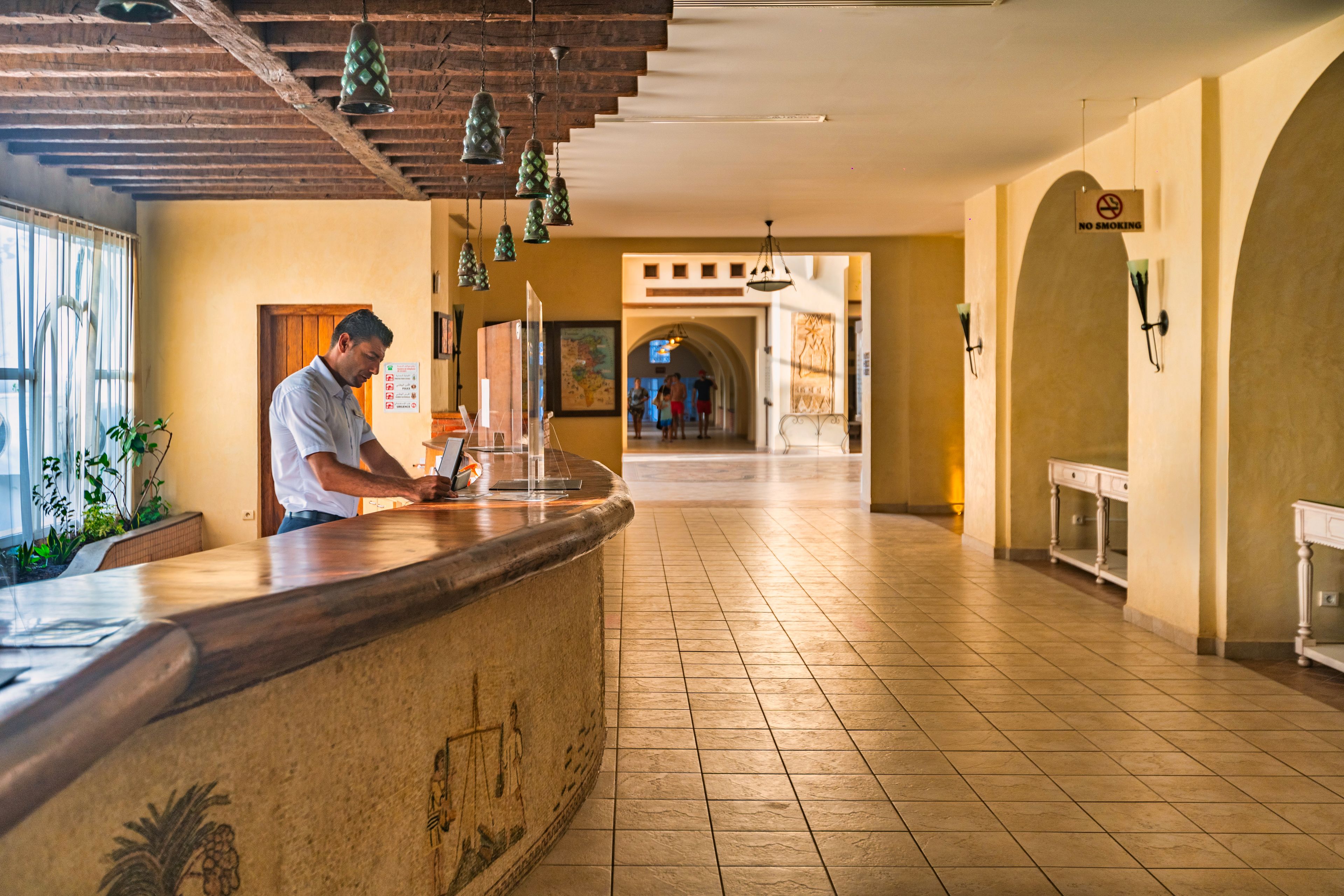 A hotel lobby with a reception desk, a map on the wall, and a staircase in the background.