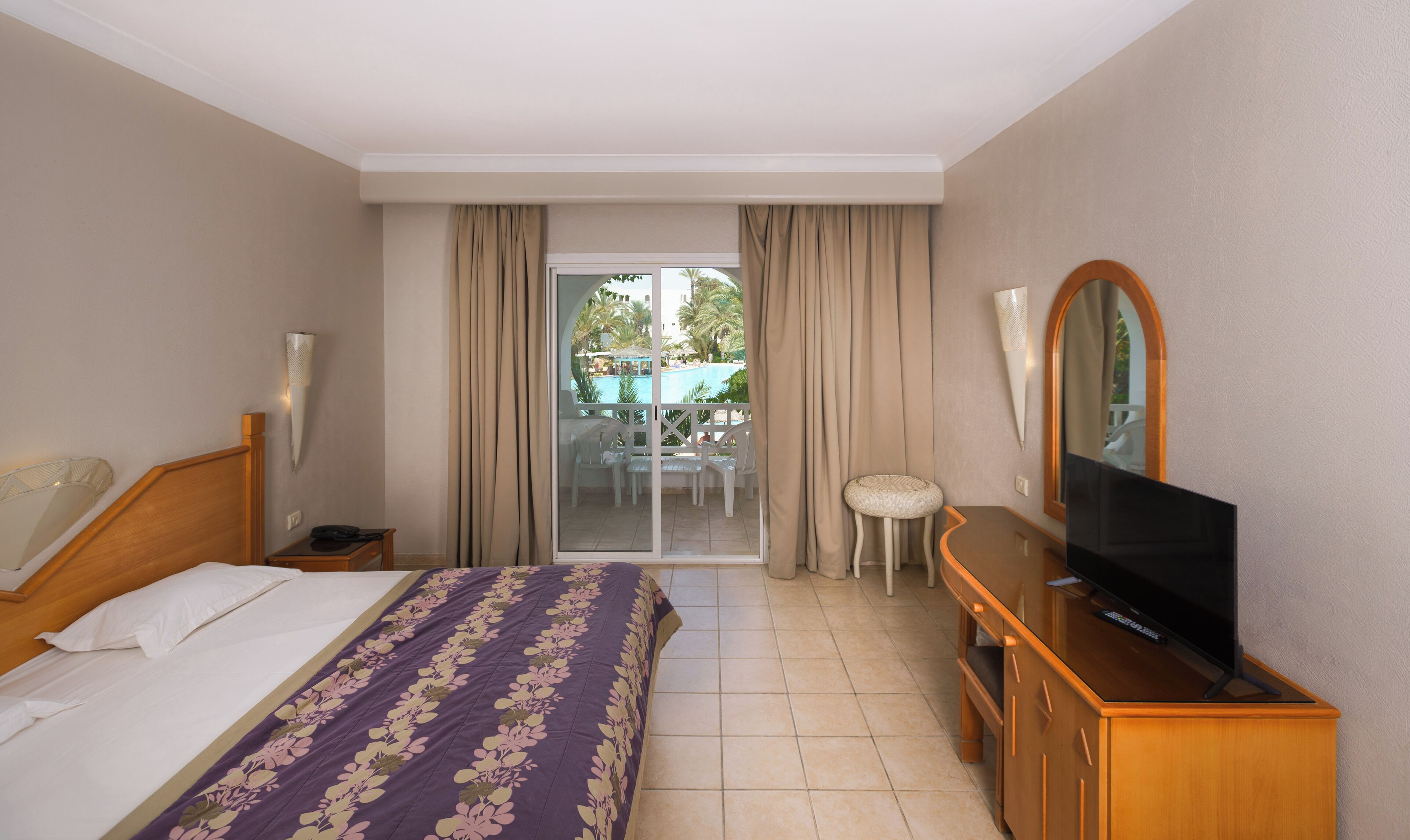 Une chambre d’hôtel avec un lit, une télévision, un bureau et un balcon donnant sur la piscine.