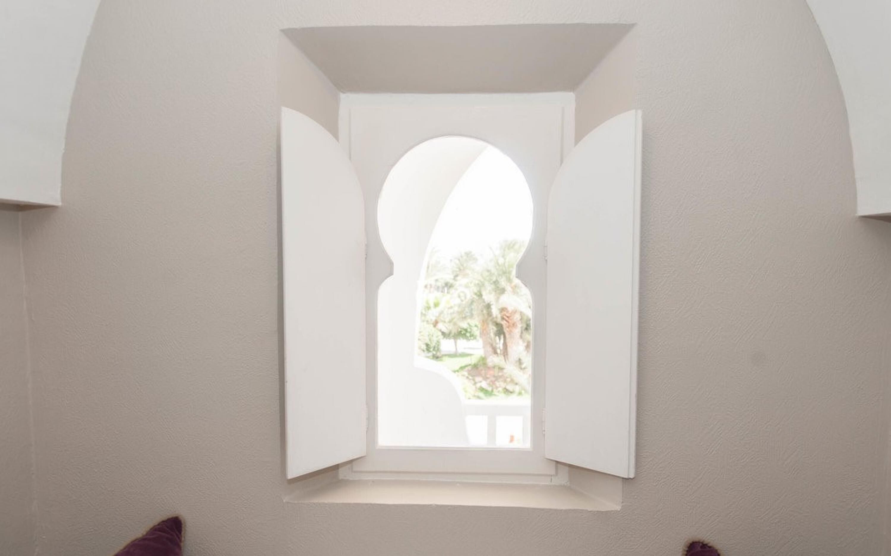 Una ventana estrecha y en arco con vista a un jardín.