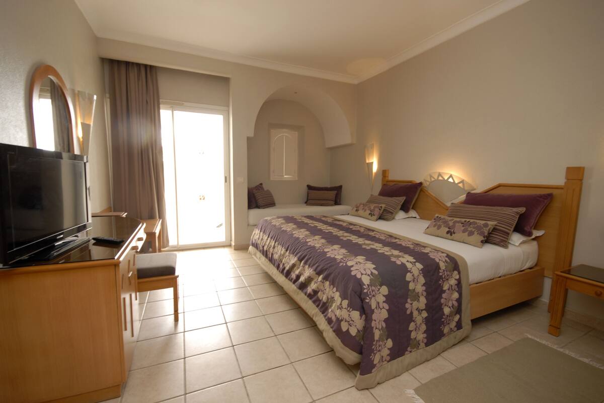 A bedroom with a bed, a TV, a desk, and a chair.