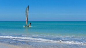 Une plage dégagée avec un voilier et une personne à bord d’un petit bateau.