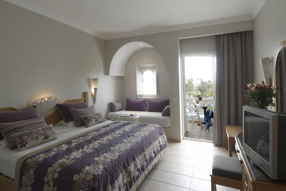 A bedroom with a bed, a TV, a desk, and a balcony with a view.