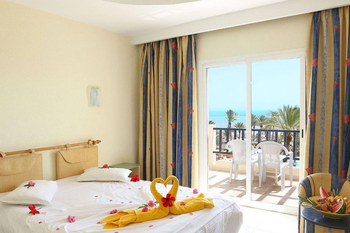 A hotel room with a bed, a balcony with a view of the sea, and a table with a fruit bowl.