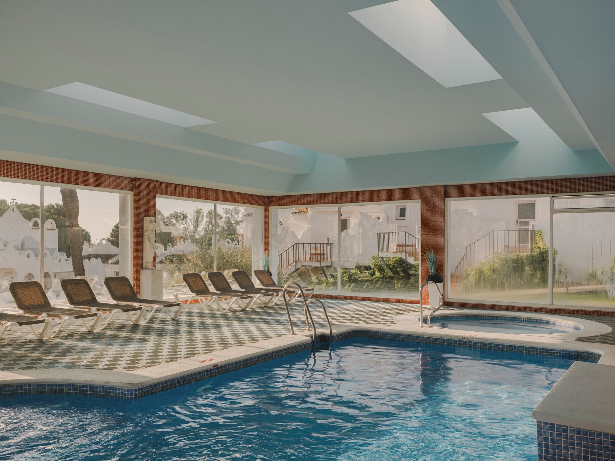 An indoor swimming pool with lounge chairs and a view of the outside.