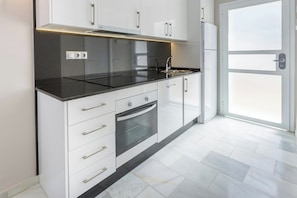 Una cocina moderna con armarios blancos, encimera negra y horno empotrado.