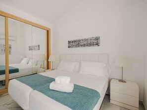 Ein Hotelzimmer mit einem großen Bett, zwei Nachttischen, einem Spiegel und Kunstwerken an der Wand.