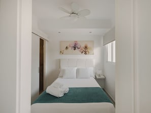 Une chambre d’hôtel avec un lit, un ventilateur de plafond, une table de chevet et une fenêtre.