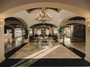 A spacious lobby with a grand chandelier, arched ceilings, and a central round table.