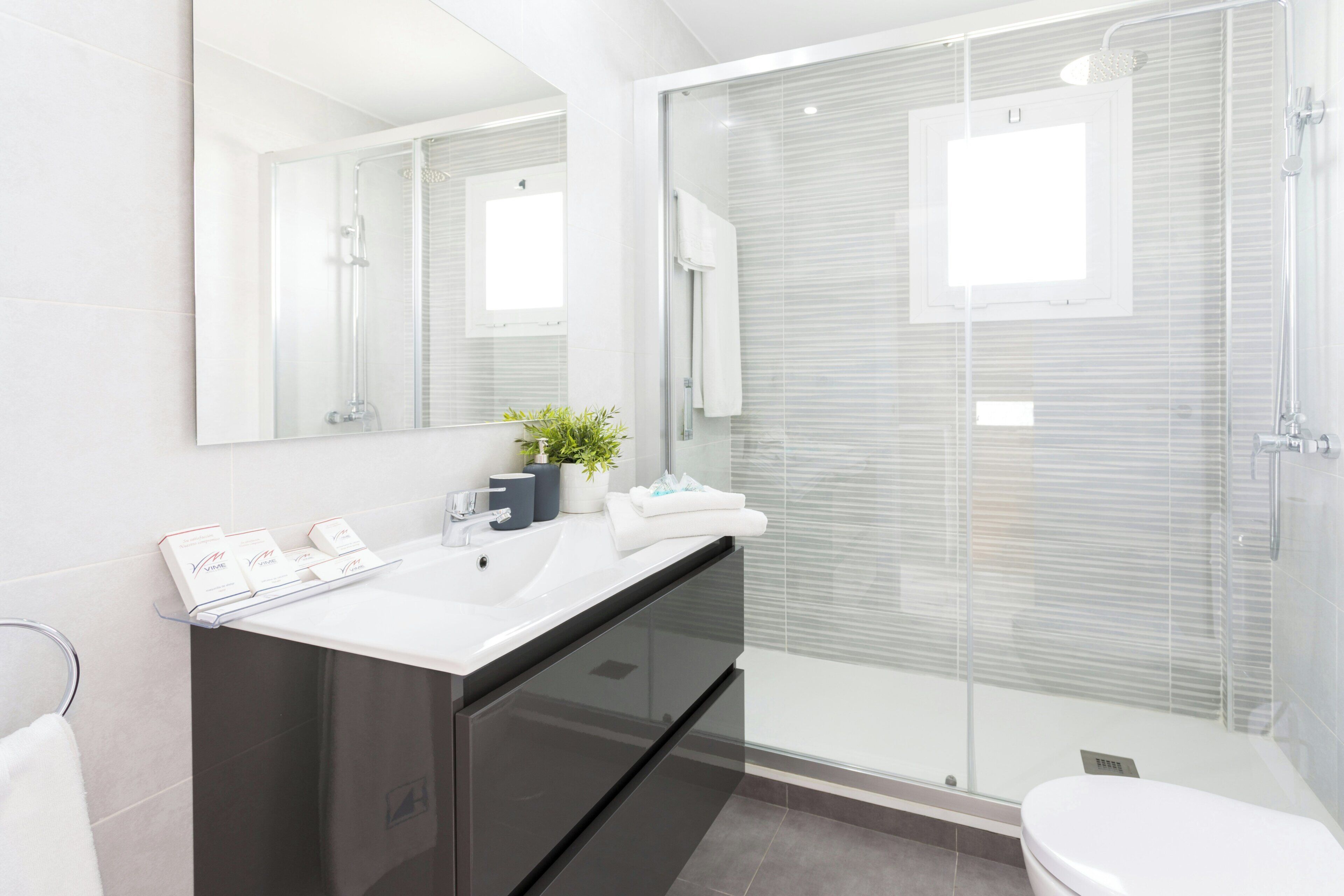 Un baño moderno con cabina de ducha de vidrio, un espejo grande y un mueble de tocador oscuro.