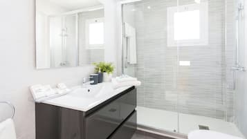 Un baño moderno con cabina de ducha de vidrio, un espejo grande y un mueble de tocador oscuro.