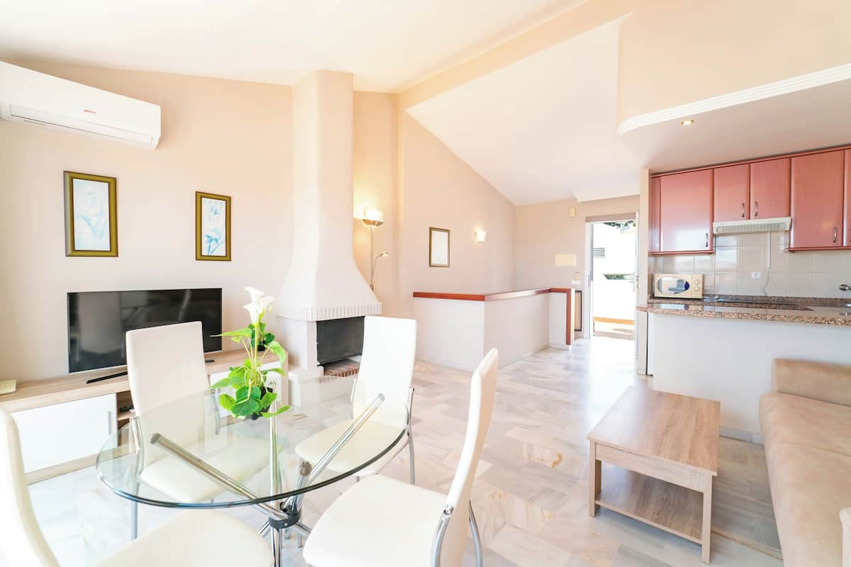 Una sala de estar moderna con una mesa de comedor de vidrio, sillas blancas, un televisor de pantalla plana y una chimenea.