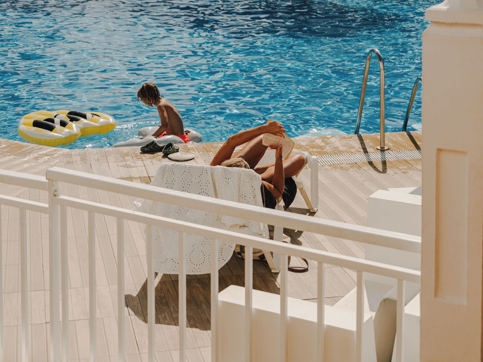A pool area with a wooden deck, a white chair, and a pool ladder.