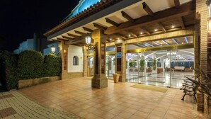Een hotelingang met een overdekt terras, betegelde vloer en een bank.