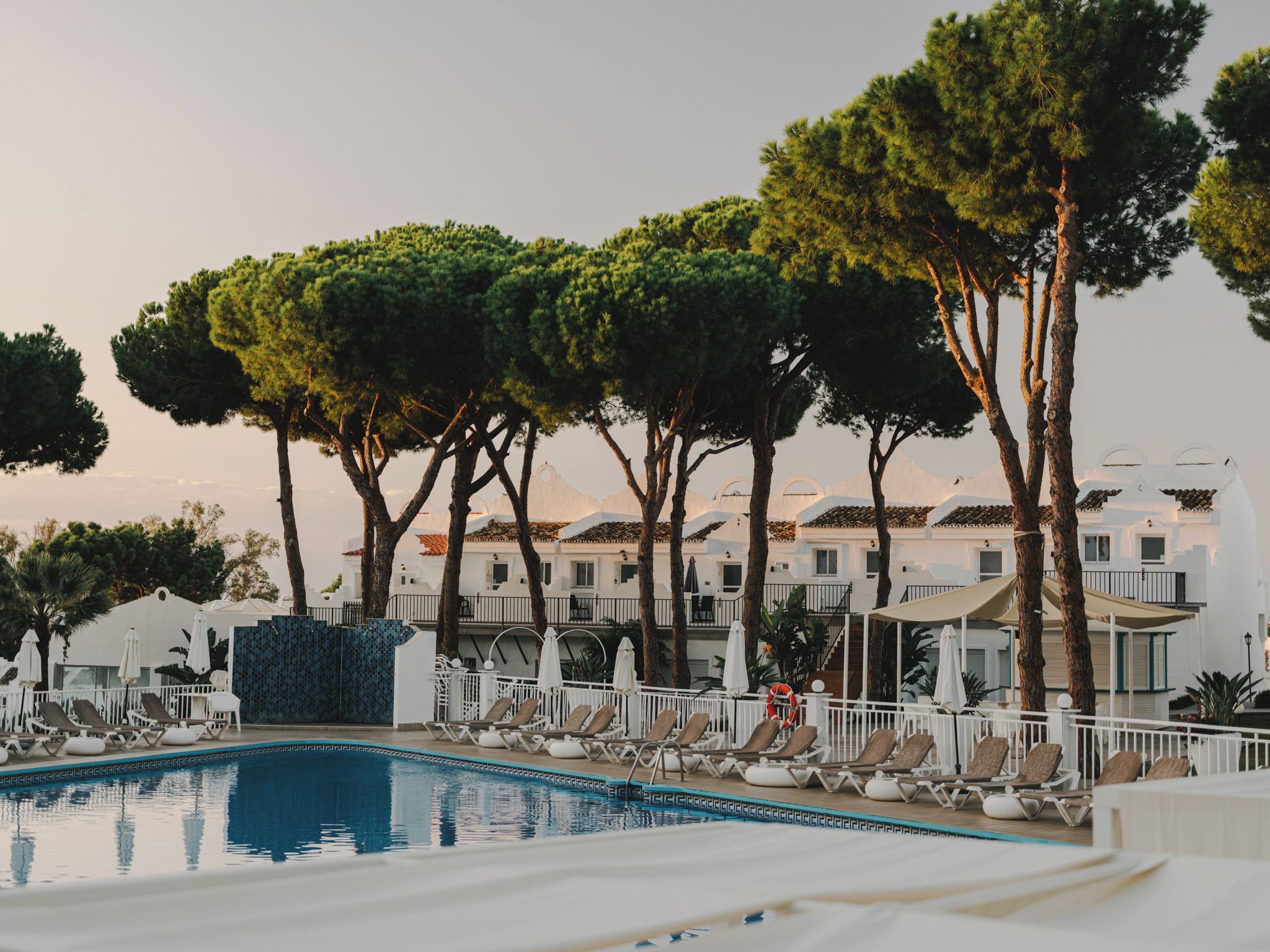 A poolside area with lounge chairs, a swimming pool, and a row of buildings with balconies.