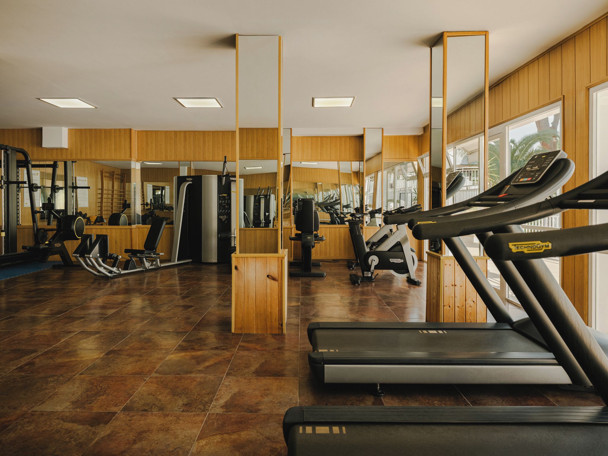 Un gimnasio con equipo de ejercicio, paredes de madera y ventanas amplias.