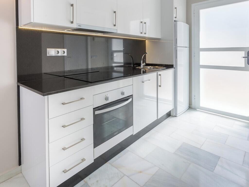 Una cocina moderna con armarios blancos, encimera negra y horno empotrado.