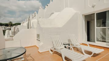 A terrace with white walls, a glass table, and two white lounge chairs.