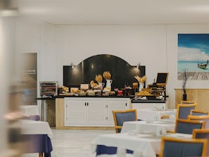 Ein Restaurant mit einer Theke, an der Speisen angeboten werden, einem Strandgemälde und gedeckten Tischen.