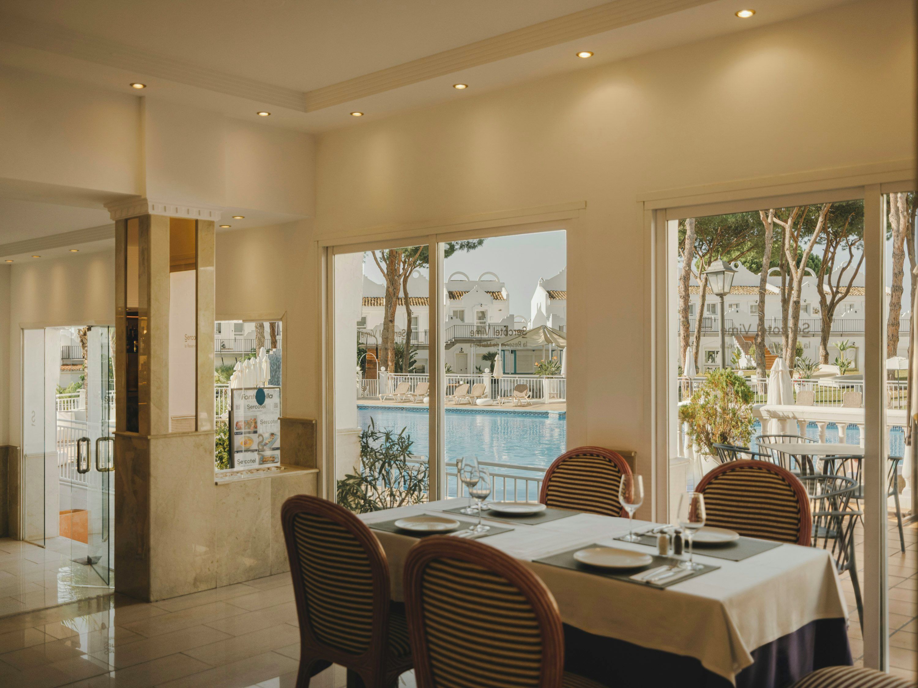A dining area with a view of a pool and buildings, featuring a table set for two with chairs.