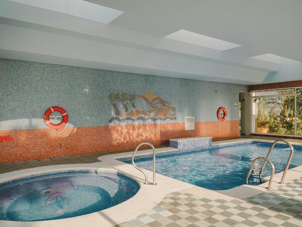 Una piscina interior con dos áreas separadas, una pared con mosaicos y una ventana que ofrece vistas a la vegetación.