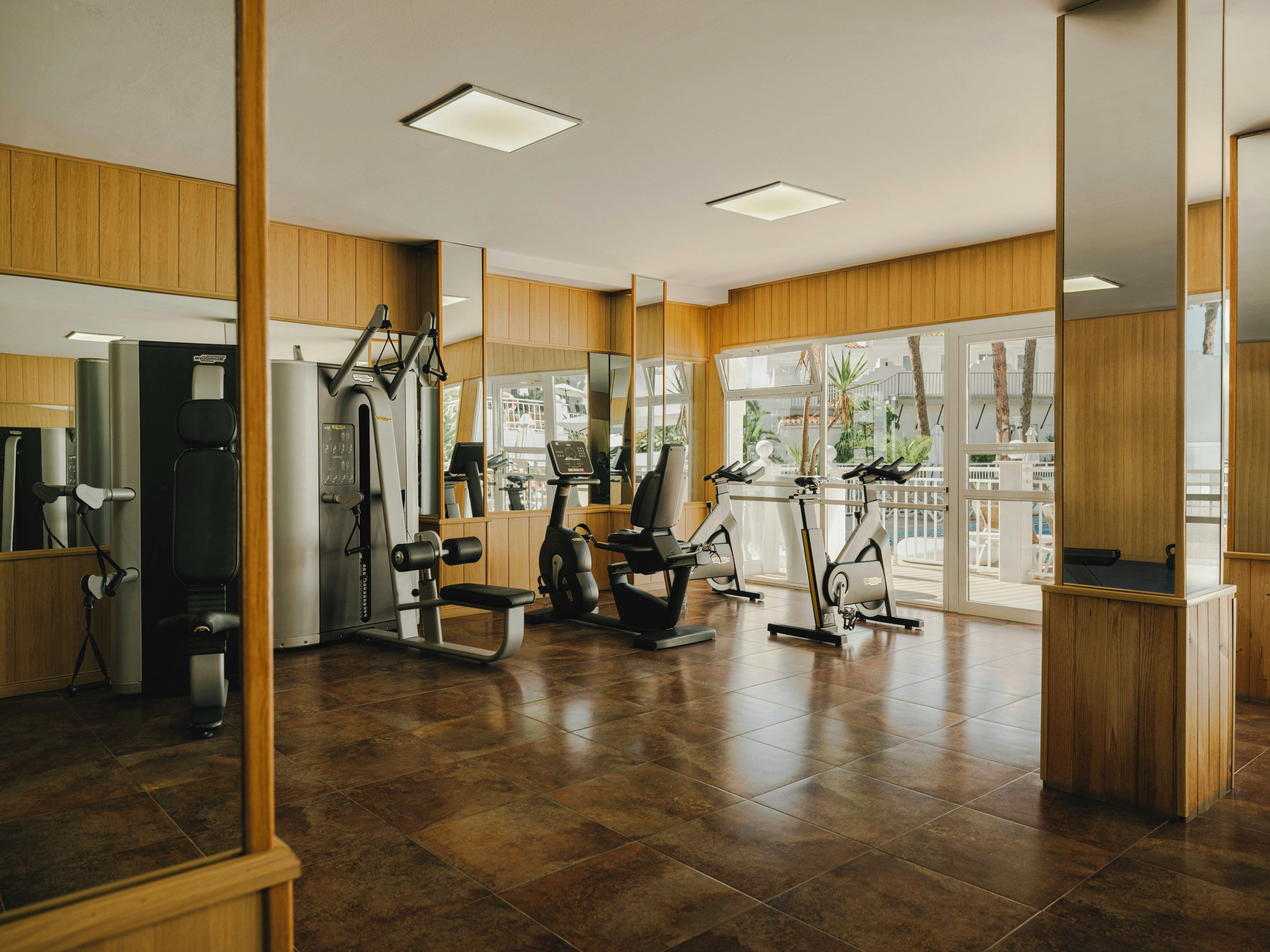 Una palestra con attrezzature per esercizi, pannelli in legno e ampie finestre.