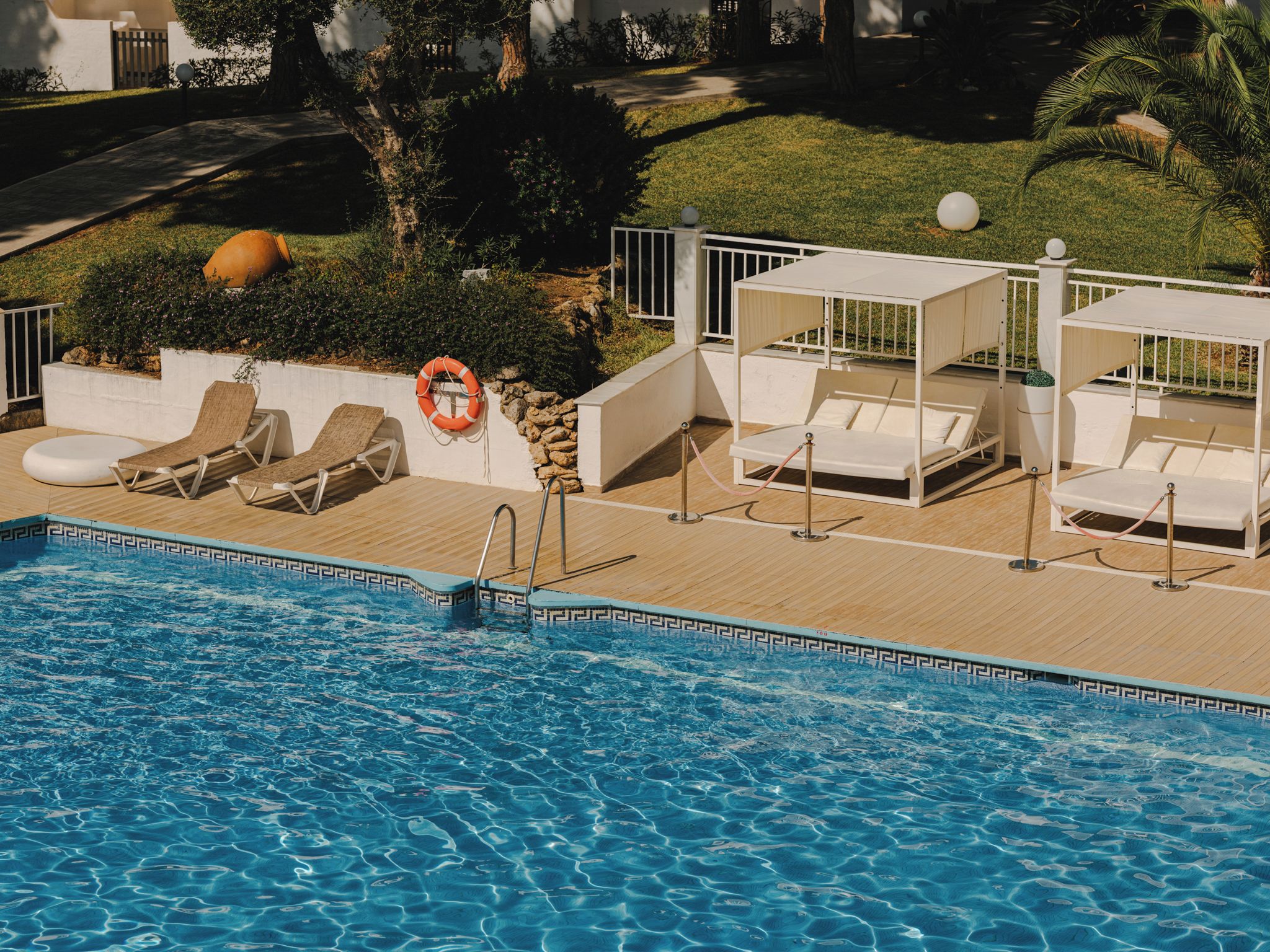 Ein Poolbereich mit Liegestühlen, einem Rettungsring und einem weißen Zaun.