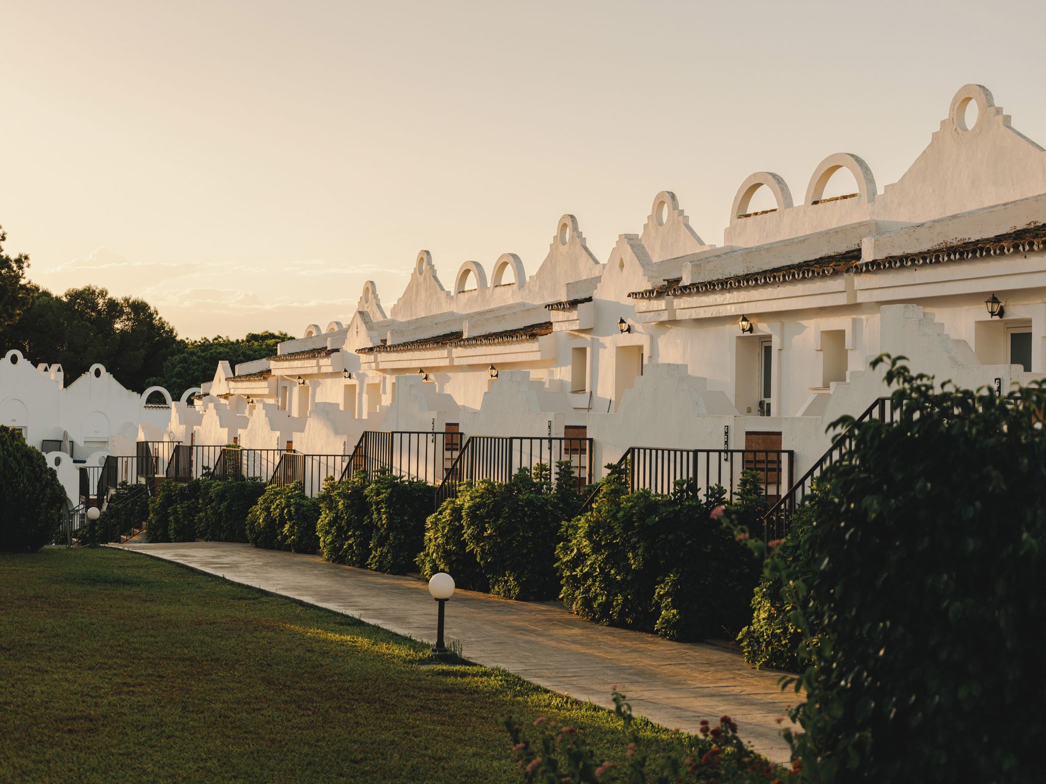 A row of white buildings with arched windows and a pathway leading to the entrance.