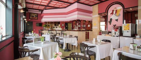 A restaurant with multiple tables and chairs, a bar area, and a ceiling with a grid pattern.