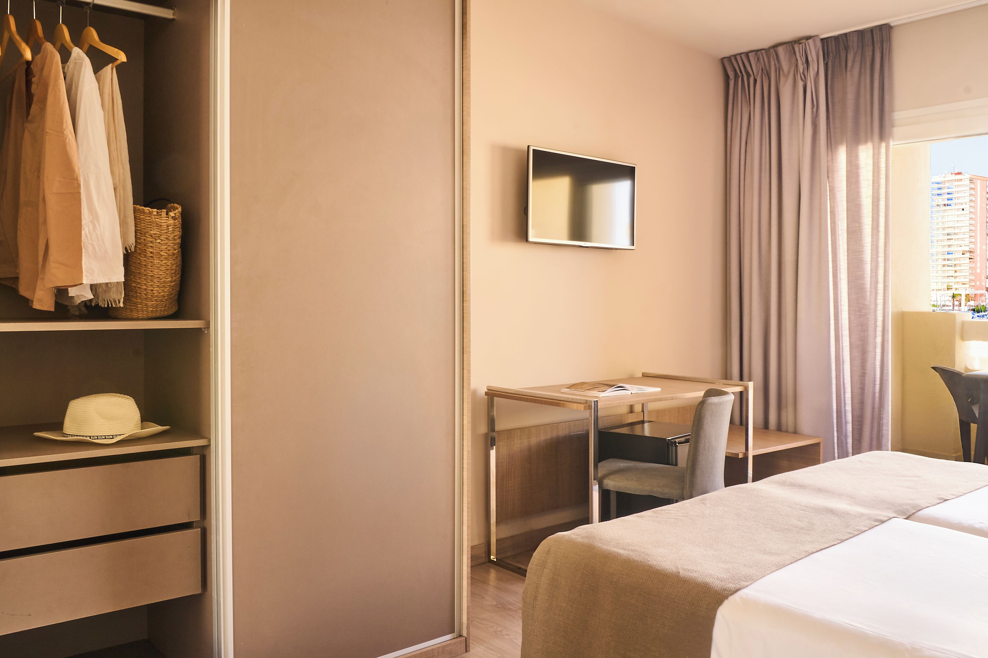 A hotel room with a bed, a desk with a chair, a wardrobe, and a television on the wall.