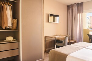 A hotel room with a bed, a desk with a chair, a wardrobe, and a television on the wall.