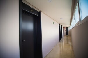 Een lange, smalle gang met links een zwarte deur waarop '404' staat, rechts een groen vertrekbord, en een betegelde vloer.