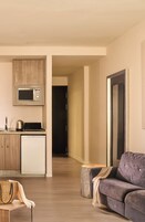 A modern living room with a sofa, a coffee table, and a kitchen area with a microwave and refrigerator.