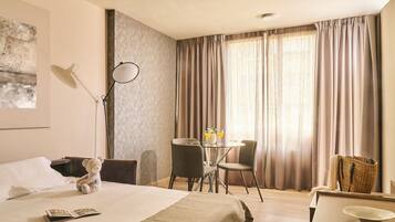Een hotelkamer met een bed, een bureau, een stoel, een lamp, een tafel met twee glaasjes water, en een teddybeer.