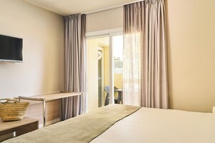 Hotelkamer met een bed, bureau, televisie en uitzicht buiten door een raam met gordijnen.