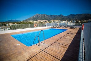 A pool area with a wooden deck, metal pool ladder, and a view of mountains in the background.