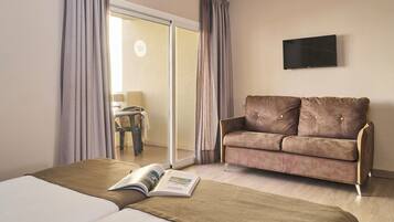 Een hotelkamer met een bed, een sofa, een televisie en een schuifdeur naar een balkon.