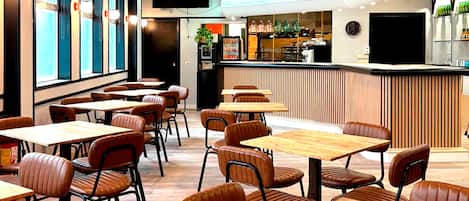 A restaurant interior with wooden tables and chairs, a counter with a beverage display, and a television mounted on the wall.