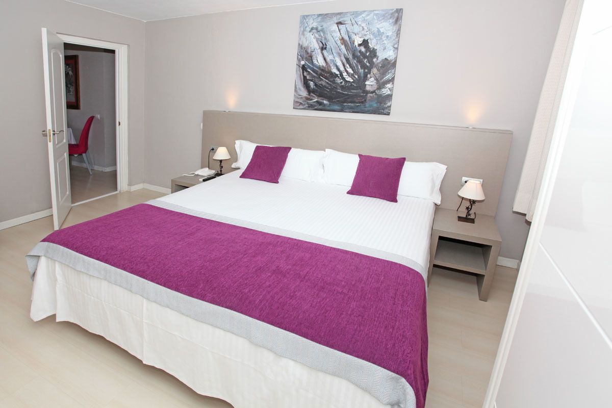 Une chambre d’hôtel avec un grand lit, deux tables de chevet, une commode, une porte donnant sur une salle de bain et un tableau au mur.