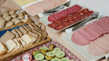 Diversos alimentos, incluindo carnes fatiadas, queijos e pão, dispostos sobre uma mesa.